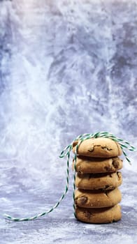 American chocolate chip cookies stacked on top of each other with green thread on a gray background. Traditional rounded crunchy dough with chocolate chips. Bakery. Delicious dessert, pastries
