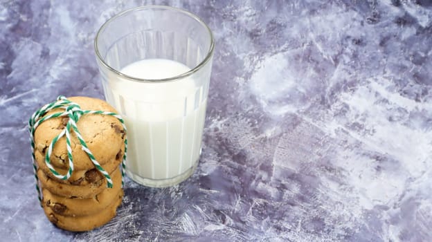 American chocolate chip cookies stacked on top of each other with milk in a glass on a gray background. Traditional rounded crunchy dough with chocolate chips. Bakery. Delicious dessert, pastries