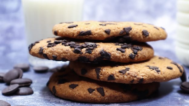 American chocolate chip cookies stacked on top of each other with milk in a glass on a gray background. Traditional rounded crunchy dough with chocolate chips. Bakery. Delicious dessert, pastries