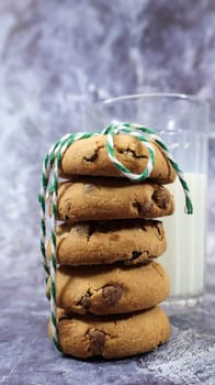 American chocolate chip cookies stacked on top of each other with milk in a glass on a gray background. Traditional rounded crunchy dough with chocolate chips. Bakery. Delicious dessert, pastries