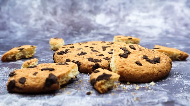 One soft freshly baked chocolate chip cookie with crumbs and chunks on a gray marble kitchen countertop. American traditional pastry, dessert. Delicious sweet food