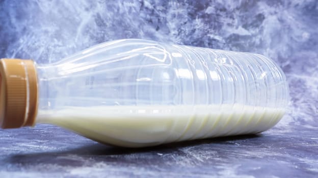 A semi-empty plastic bottle of fresh regular milk lies on a dark gray marble or concrete backdrop. Close-up front view. World milk day concept. Nutrient fluid