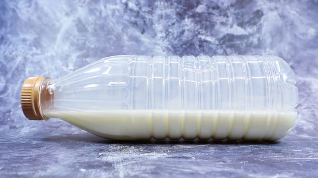 A semi-empty plastic bottle of fresh regular milk lies on a dark gray marble or concrete backdrop. Close-up front view. World milk day concept. Nutrient fluid