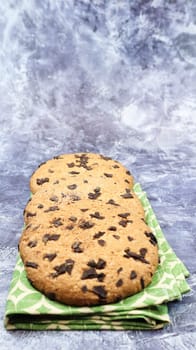 American chocolate chip cookies on a green napkin on a gray background. Traditional round crispy dough with chocolate chips. Bakery. Delicious dessert, pastries. Vertical photography.