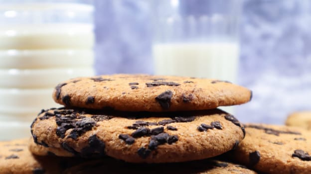 American chocolate chip cookies stacked on top of each other with milk in a glass on a gray background. Traditional rounded crunchy dough with chocolate chips. Bakery. Delicious dessert, pastries