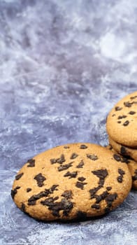 Soft, freshly baked chocolate chip cookies on a gray marble kitchen countertop. American traditional sweet pastry pastry, delicious homemade dessert. Culinary background. Vertical photography.