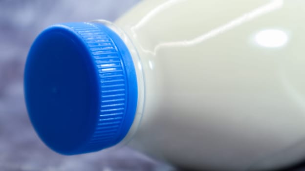 A plastic bottle with a blue cap of fresh regular milk on a dark gray marbled or concrete background. Close-up front view. World milk day concept. Nutrient fluid