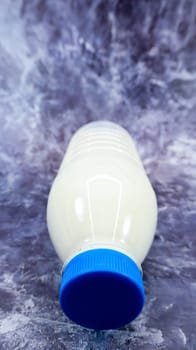 A plastic bottle of fresh regular milk on a dark gray marbled or concrete background. Close-up front view. World milk day concept. Nutrient fluid. Vertical photography