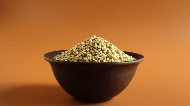 Raw green buckwheat in a brown clay plate on a brown background. Vegan organic food concept. The concept of diet, weight loss, healthy and proper nutrition. Copy space for text or logo