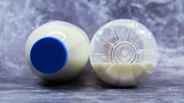 A half-empty and full plastic bottle of fresh regular milk lies on a dark gray marble or concrete backdrop. Close-up front view. World milk day concept. Nutrient fluid