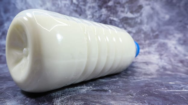 A plastic bottle with a blue cap of fresh regular milk on a dark gray marbled or concrete background. Close-up front view. World milk day concept. Nutrient fluid