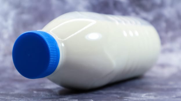 A plastic bottle with a blue cap of fresh regular milk on a dark gray marbled or concrete background. Close-up front view. World milk day concept. Nutrient fluid