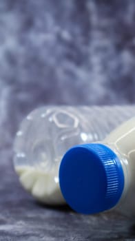 A plastic bottle of fresh regular milk on a dark gray marbled or concrete background. Close-up front view. World milk day concept. Nutrient fluid. Vertical photography