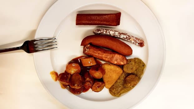 Assorted German sausages on a white plate with a fork in a pub. Traditional German food in a plate. Carrivurst, Bratwurst, Thuringian, Weisswurst, Nuremberg, Bockwurst, Nekvurst.