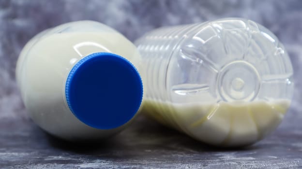 A half-empty and full plastic bottle of fresh regular milk lies on a dark gray marble or concrete backdrop. Close-up front view. World milk day concept. Nutrient fluid