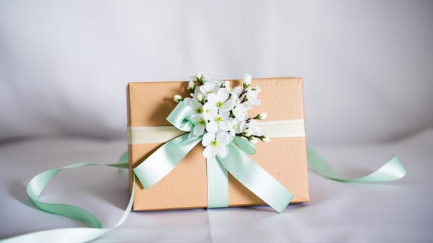 The gift comes in minimalist packaging, decorated with a neutral, calm blue ribbon and flowers symbolizing the arrival of spring. High quality photo