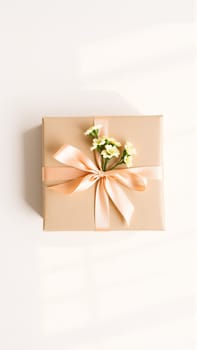 The gift is packaged in minimalist packaging, decorated with a neutral, calm ribbon in nude tones and flowers symbolizing the arrival of spring. High quality photo