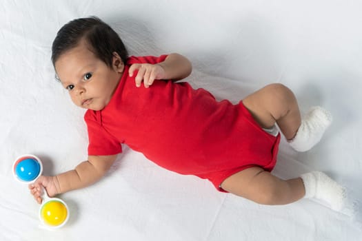 Infant lying on his back wearing red clothes holding a toy in his hand