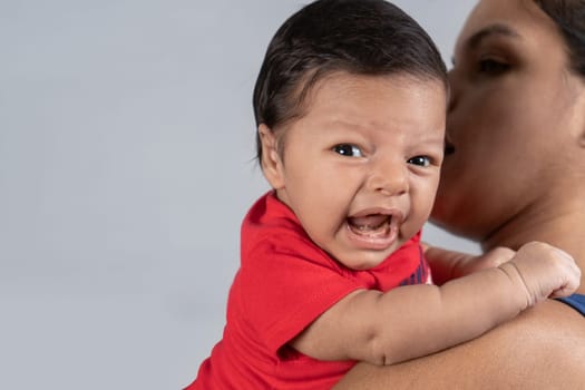 Infant with crying expression, carried in the hands of a woman