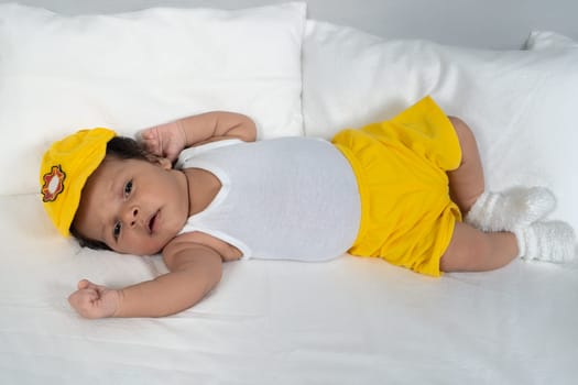Infant lying on his back wearing a white t-shirt and yellow shorts