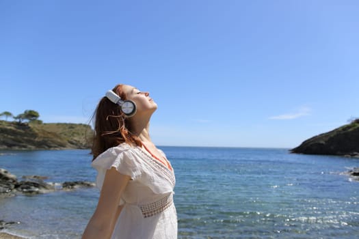Profile of a ldy meditating breathing fresh air with wireless headphones on the beach