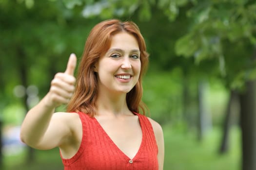 Happy woman gesturing thumbs up looking at camera in a park