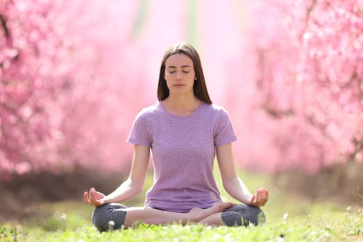 Front view portrait of a relaxed woman practicing yoga in a beautiful pink field