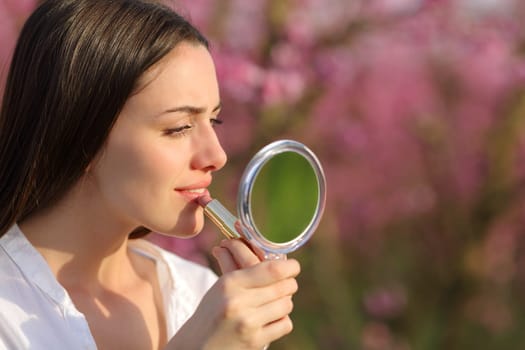 Beautiful concentrated woman painting lips using mirror in a pink field