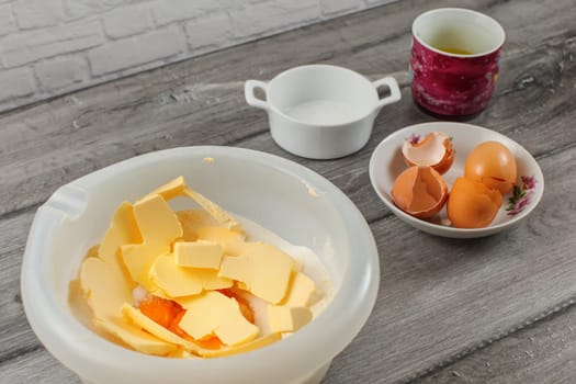 Cake preparation - plastic bowl with flour and yolk, egg shells and salt in background on gray wood table.