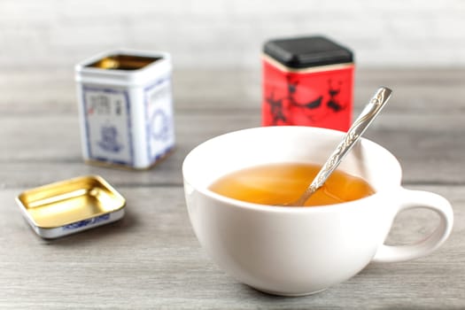 Cup of hot black tea, with metal loose leaf caddy in back, on gray wood desk.