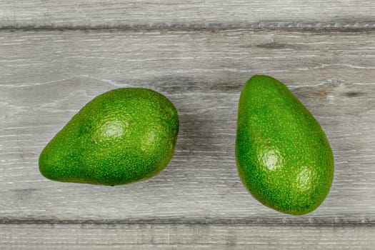 Table top view - two whole avocado fruits on gray wood desk.
