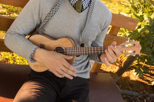 young man playing ukulele sitting on bench outdoors