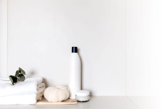 White bathroom shelf with different bath accessories. Hotel cleaning concept. Household concept. Washcloth, shampoo, cream, plant, toothbrush, brush, eucalyptus leaves on white towels. Body, skin care
