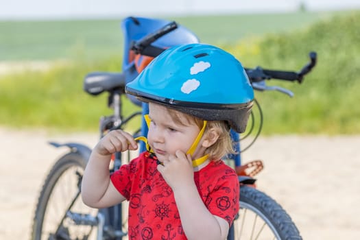 Little boy adjusts his blue safety bicycle helmet. All potential trademarks are removed.