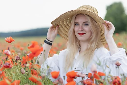 Portrait of smiling young woman holding her straw hat posing in red poppy field smiling at the camera. Horizontally.
