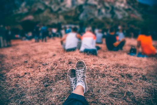 Teens at concert at summer festival. Legs of teenager at summer music festival, canvas shoes, sitting on the grass in front of stage