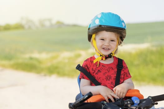 Smiling little boy with safety helmet on the head is posing in bicycle seat. All potential trademarks are removed.
