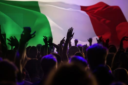 Football fans supporting Italy - crowd celebrating in stadium with raised hands against Italy flag