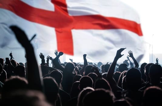 Football fans supporting England - crowd celebrating in stadium with raised hands against England flag