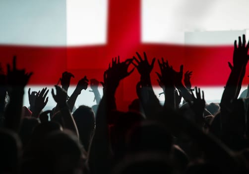 Football fans supporting England - crowd celebrating in stadium with raised hands against England flag