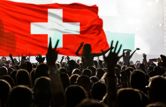 Soccer fans supporting Switzerland - crowd celebrating in stadium with raised hands against Switzerland flag