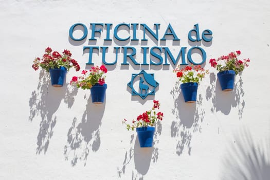 Cabra, Spain - May 19th, 2019: Cabra tourist office whitewashed wall full of attached blue flower pots, Cordoba, Spain. Typical andalusian architecture background