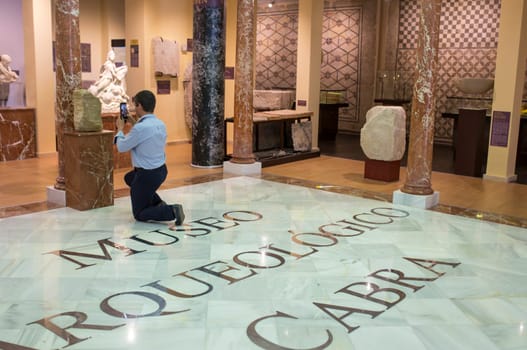 Cabra, Spain - May 19th, 2019: Man on knees taking picture in museum. Archaeological Museum of Cabra Main Hall, Cordoba, Spain