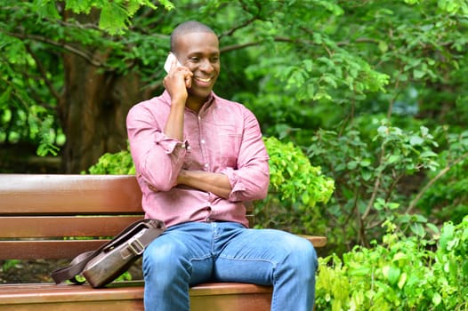 Casual man sitting on park bench and talking on cell phone
