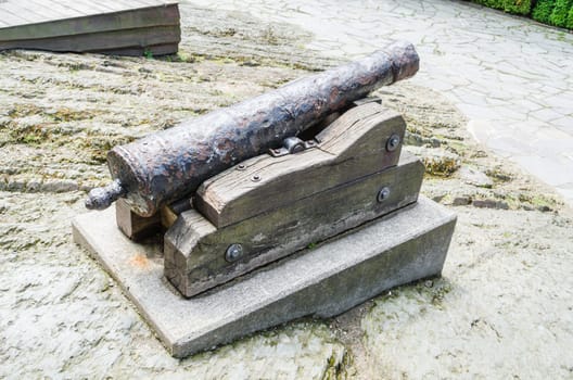 Antique cannon stands on the pier with paved paving stones against the background of the forest. Old cannon large. Ancient black cannon.