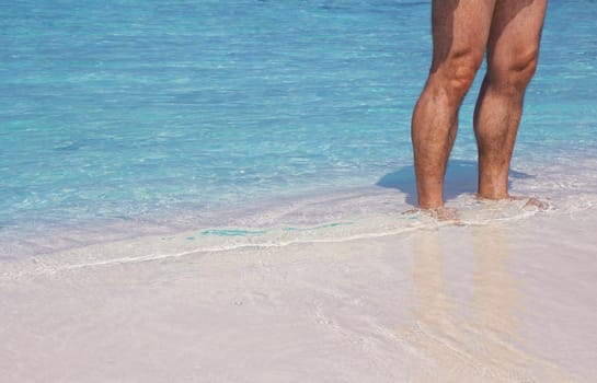 A man stands in the warm sandy beach in front of the blue sea