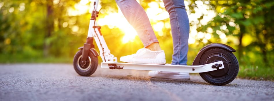 Woman riding on scooter in park in summer. Urban eco transportation