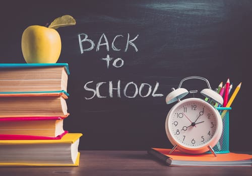 school accessories on the table with blackboard background. Pencils and books