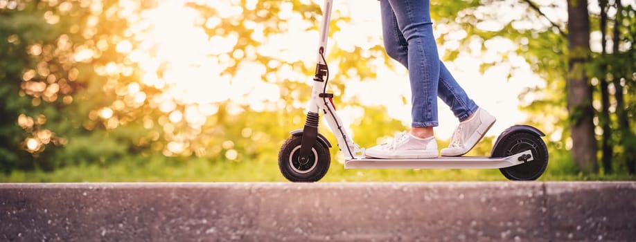 Woman riding on scooter in park in summer. Urban eco transportation