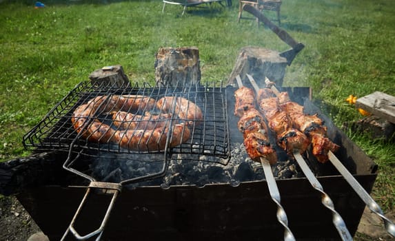 Man preparing shashlik or shish kebab over charcoal. Barbeque meat and sausages or bratwurst on a grill grate in backyard. Grilled meat on metal skewer outdoor. BBQ party or picnic food. Close up shot